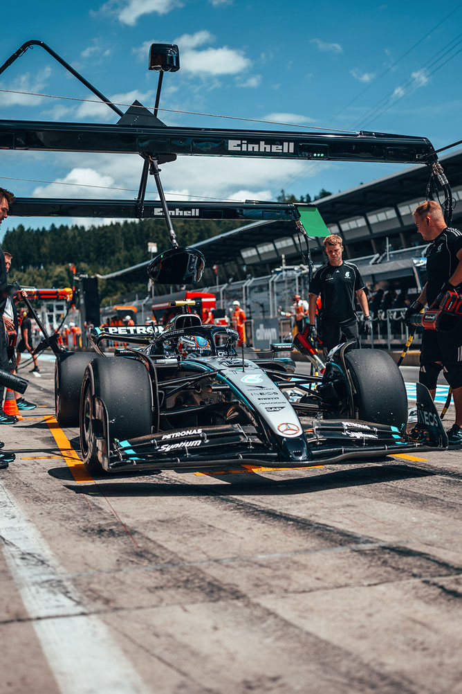 Mercedes-AMG Formula 1 -auto on varikkokäytävällä, tiimin jäsenten ympäröimänä Einhell-tallin rakenteiden alla.